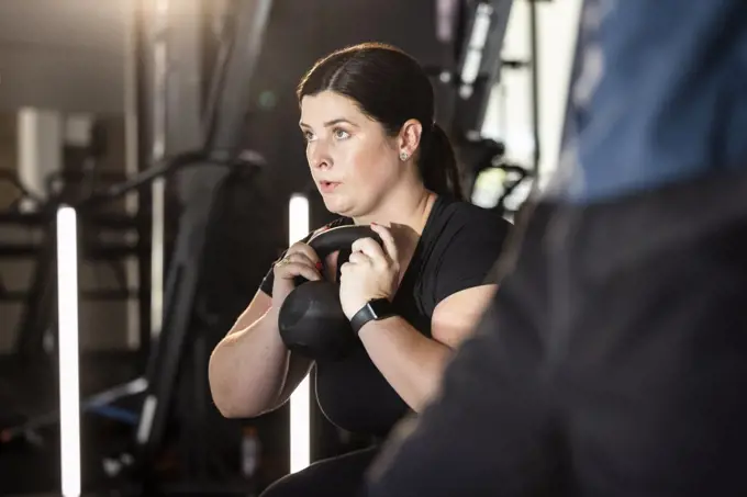 Woman working out in gym doing dumbbell squat                       