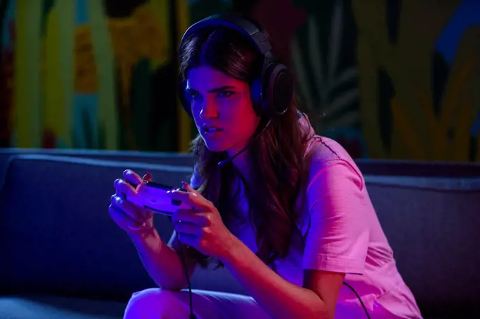 Woman with game controller sitting in front of TV wearing microphone headset with intensity.