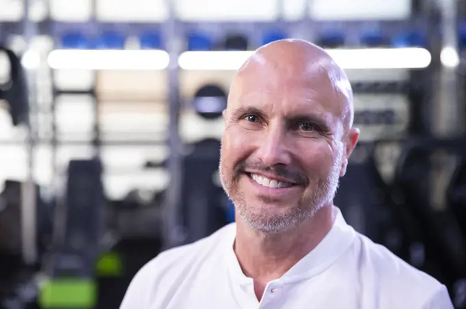 Portrait of a bald fitness trainer at a gym smiling into camera.