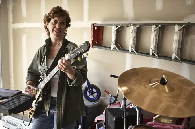 Portrait of guitar player in Garage band composed of middle aged women, practicing in residential garage 