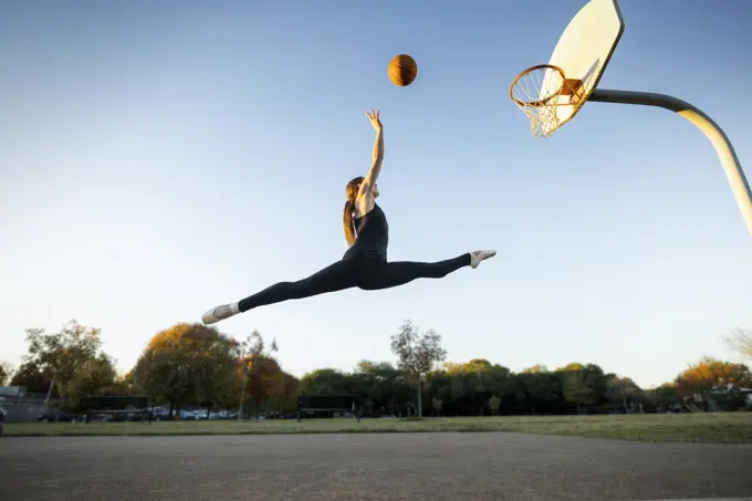 Female ballet dancer shooting baskets on an outdoor Basketball court 