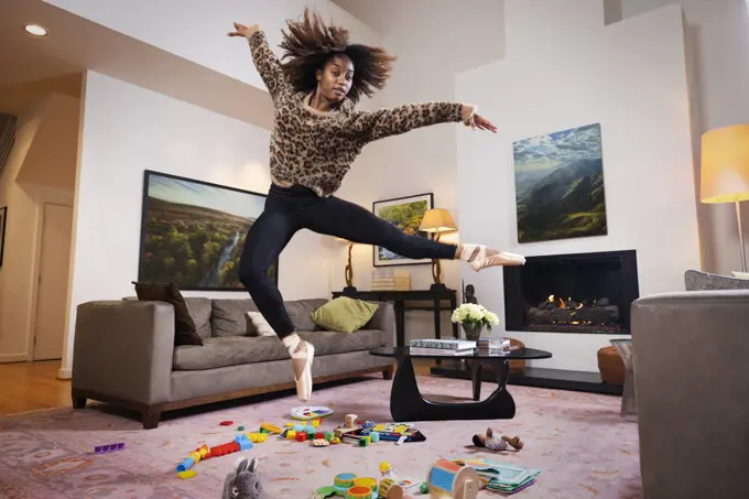 Mother and Ballet dancer jumping over kids toys on floor in living room