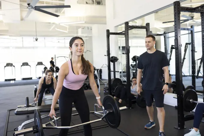 Young woman in brightly lit gym look straight ahead and doing deadlifts with trap bar. deadlift