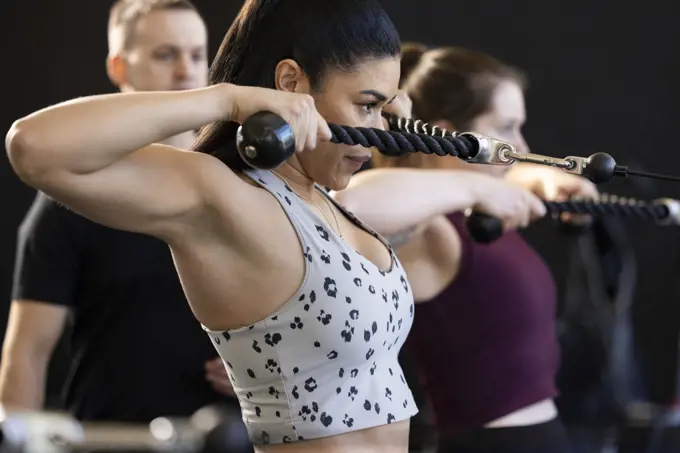 Side view of a determined young woman looking straight ahead using a cable pulley machine in gym