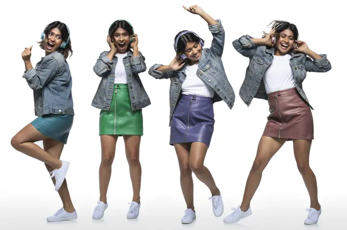 Lifestyle portrait of young woman wearing leather mini skirt and denim jacket with headphones and dancing on white background 