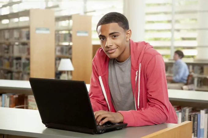 Portrait of African American student in library using laptop to study. 