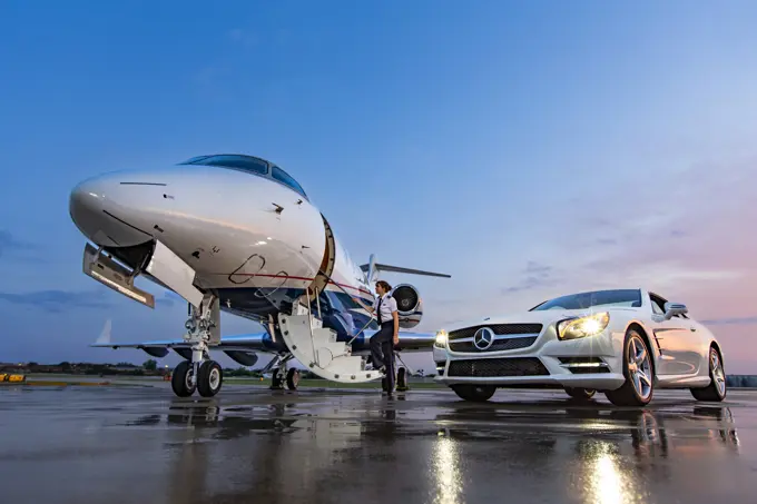 Female Pilot boarding Jet on tarmac of small airport, Mercedes sports car  parked next to plane 