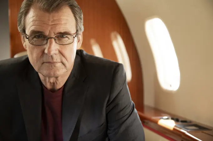 Portrait of mature business man  wearing glasses sitting in seat aboard private jet 