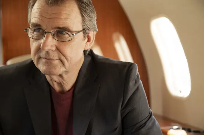 Portrait of mature business man  wearing glasses sitting in seat aboard private jet looking off camera 