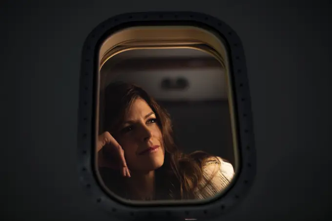 Low angle close up portrait of Middle aged  woman sitting n cabin of private plane looking out of window with contemplative look, view from outside of plane  