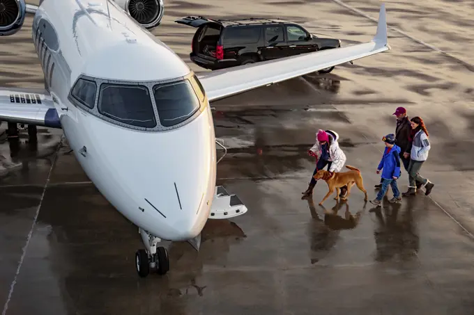 High angle view of Family with dog boarding private plane on wet tarmac of private airport for family vacation 