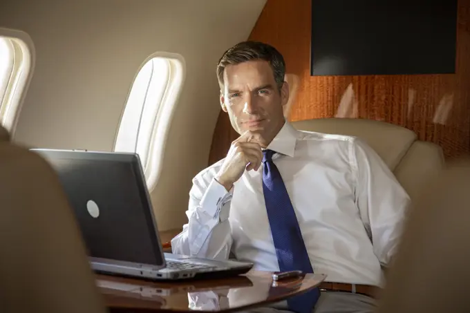 Portrait of smiling businessman in cabin of  private jet  with laptop computer 