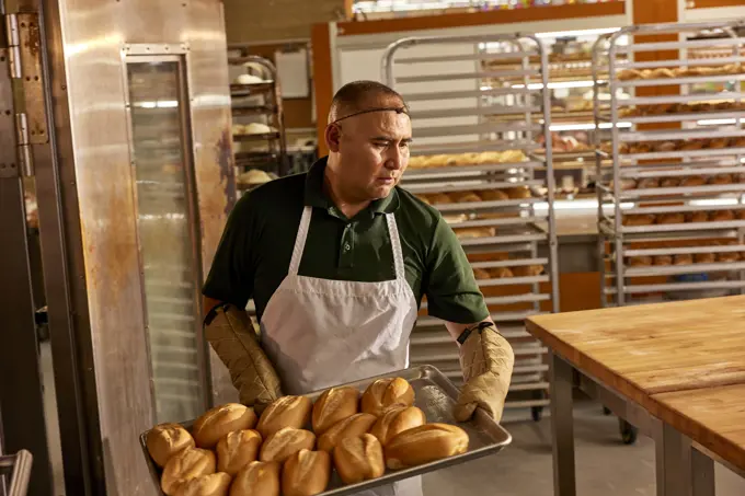 baker in kitchen of grocery store removing tray of Bolillos from oven. (a type of savory bread made in Mexico and Central America)