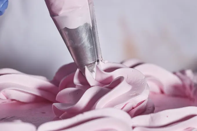 Close up detail of piping bag adding strawberry buttercream flowers and cake border accents to chocolate layer cake