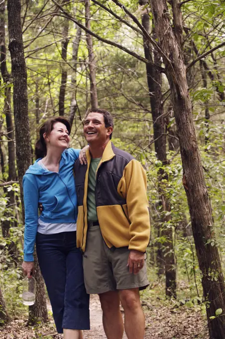 Older couple  hiking arm in arm on trail through the woods, smiling and laughing