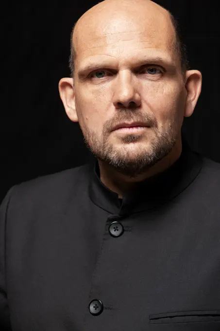 Close up portrait of conductor Jaap van Zweden looking directly to camera  in spotlight on black background at The Morton H. Meyerson Symphony Center,  Orchestra concert hall located in the Arts District of downtown Dallas, Texas. portraying the intense concentration of a conductor, whose stern expression captures the gravity of leading a musical performance.