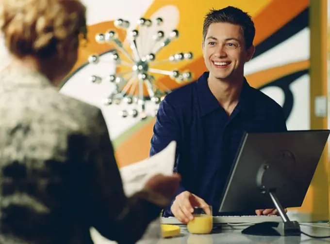 Teenage boy using a desktop PC with a woman reading a newspaper