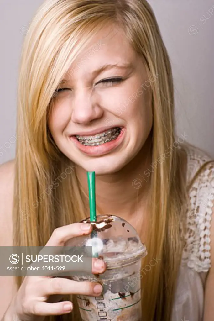 Teenage girl wincing from a brain freeze while drinking iced coffee