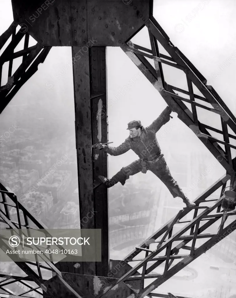 Worker painting the Eiffel Tower. Working without a safety harness he precariously straddles steel beams. The tower is being repainted in three colors: Yellow-Orange on top, Yellow -brown in the middle, and dark yellow at bottom. March 28, 1953.