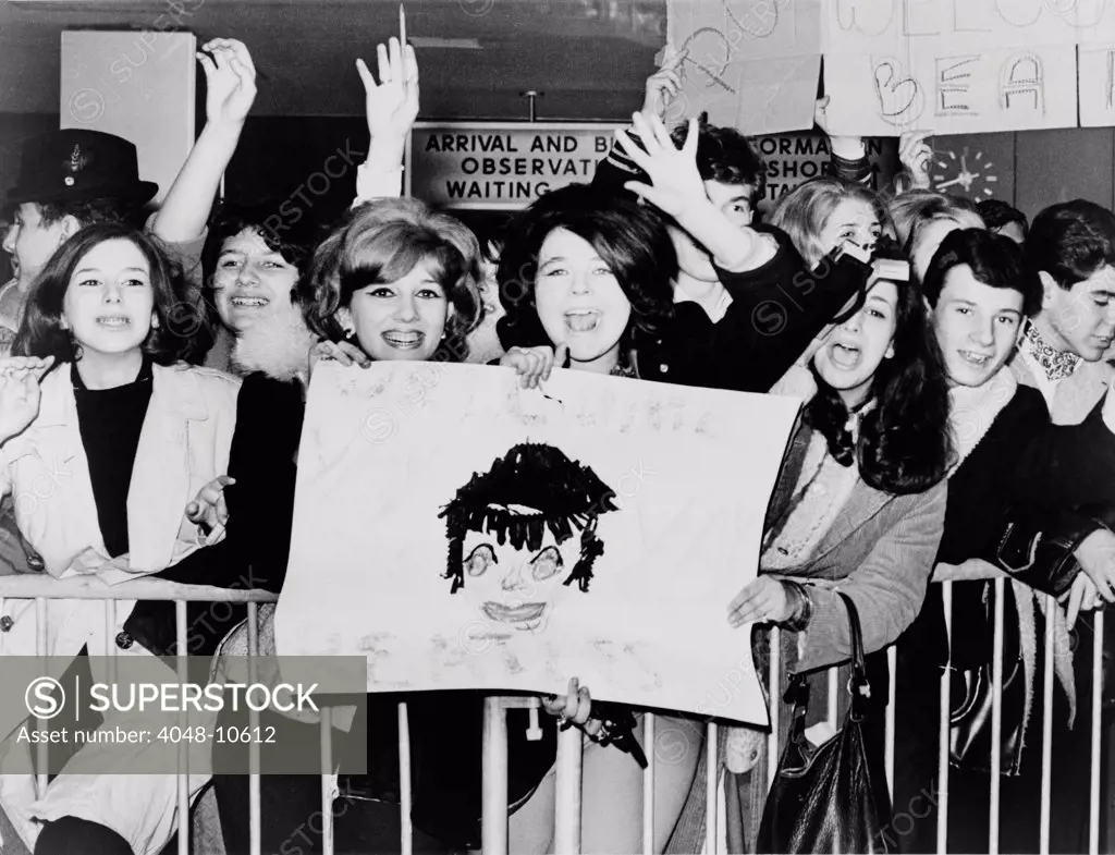 Screaming teenagers girls wave a crude sign as they welcome 'The Beatles' at New York's Kennedy Airport. Feb. 7, 1964.