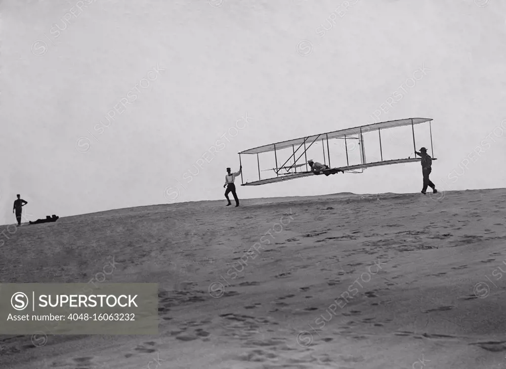 Wright Brothers' glider with a single vertical rudder before its flight, Oct. 10, 1902. Orville lies prone in glider as Wilbur and Dan Tate hold the wing tips at left and right. Kitty Hawk, North Carolina  (BSLOC_2018_2_143)