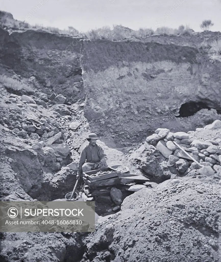 Gold prospector working a rocker box near Virginia City, Montana Territory, in 1871. He pours water over the gravel in the top box, which when rocked back and forth will help to separate heavier gold dust from the sand and gravel. The device doubled the pace at which gold bearing gravel worked. Photo by William Henry Jackson, 1871  (BSLOC_2020_1_39)