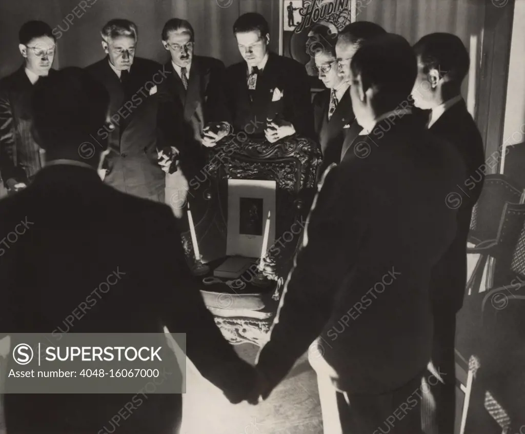 Thirteen magicians clasping hands in a midnight séance to contact the deceased Harry Houdini, on Halloween, 1946. To no avail, they arranged a Houdini's portrait, two candles, a book, and handcuffs, on a chair  (BSLOC_2020_2_21)