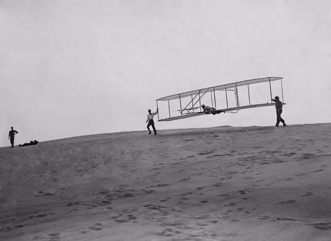 Wright Brothers' glider with a single vertical rudder before its flight, Oct. 10, 1902. Orville lies prone in glider as Wilbur and Dan Tate hold the wing tips at left and right. Kitty Hawk, North Carolina  (BSLOC_2018_2_143)