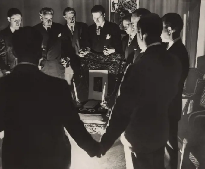 Thirteen magicians clasping hands in a midnight séance to contact the deceased Harry Houdini, on Halloween, 1946. To no avail, they arranged a Houdini's portrait, two candles, a book, and handcuffs, on a chair  (BSLOC_2020_2_21)