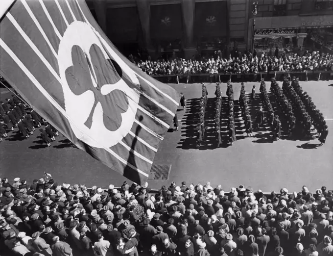 Flag with shamrock flies above Fifth Avenue as Saint Patrick's Day Parade passes below, New York City in 1961.