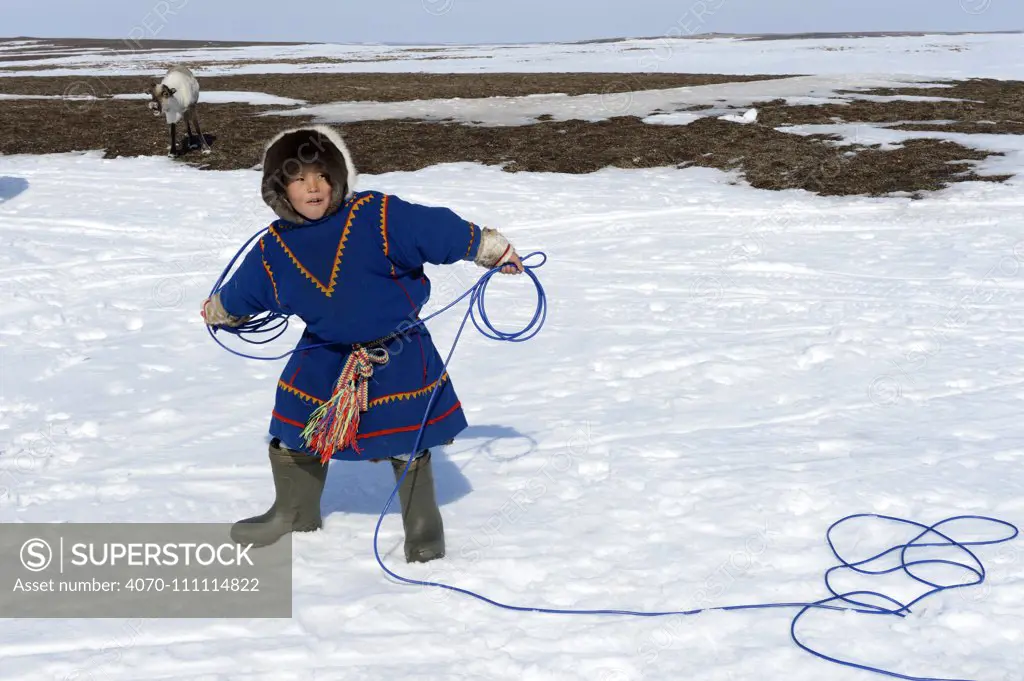 Young boy, Nenet herder practising lasso, wearing traditional malitsa coat. Yar-Sale district, Yamal, Northwest Siberia, Russia. April 2016.