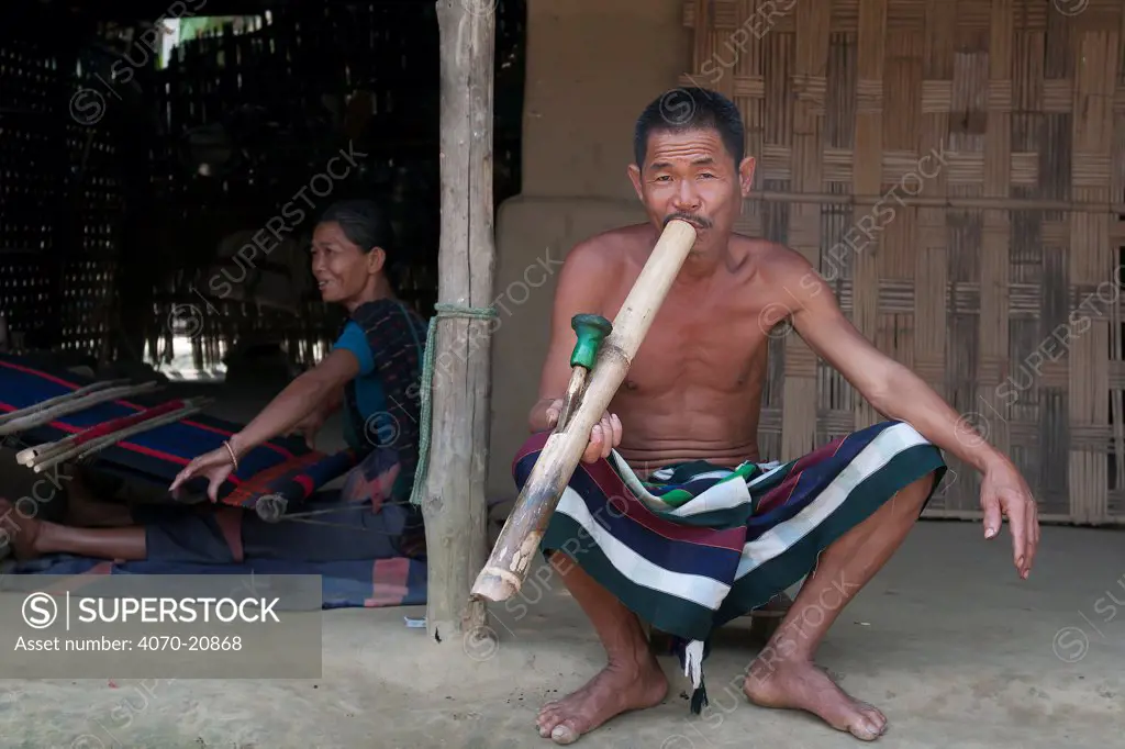 Stock photo of Man of Chakma tribe, smoking a bamboo pipe (daba), with  woman weaving on…. Available for sale on