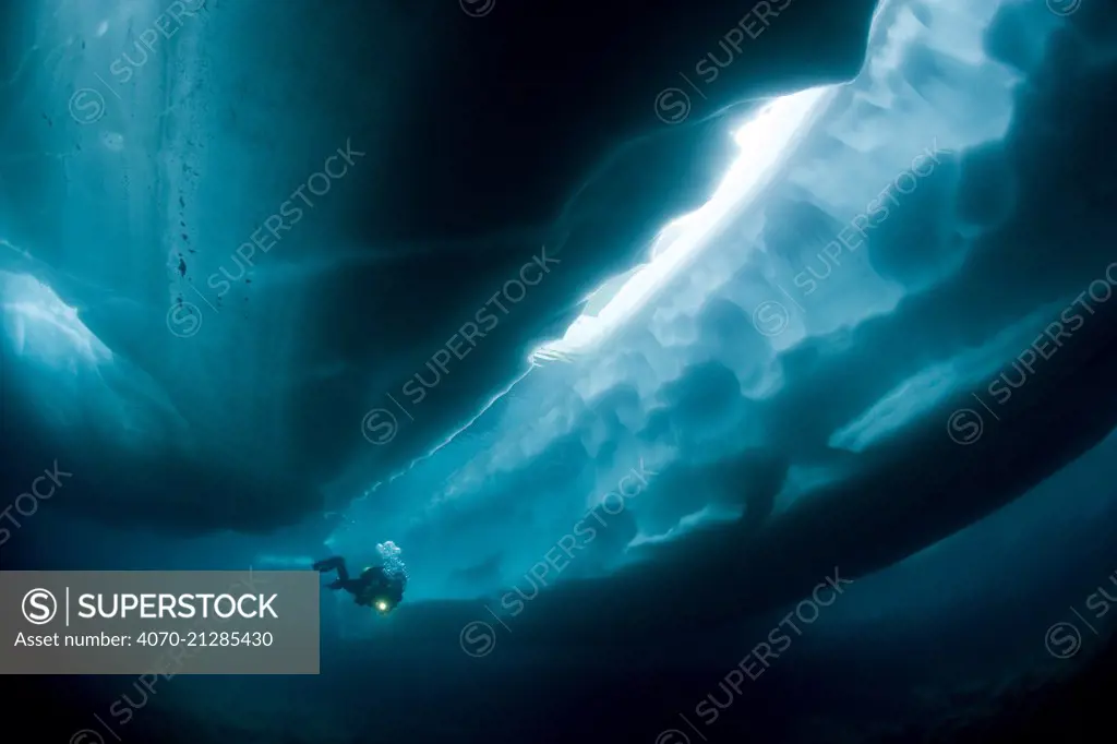 Scuba diver under and between ice formations, Lake Sassolo, Sambuco valley, Ticino, Switzerland. Model released.