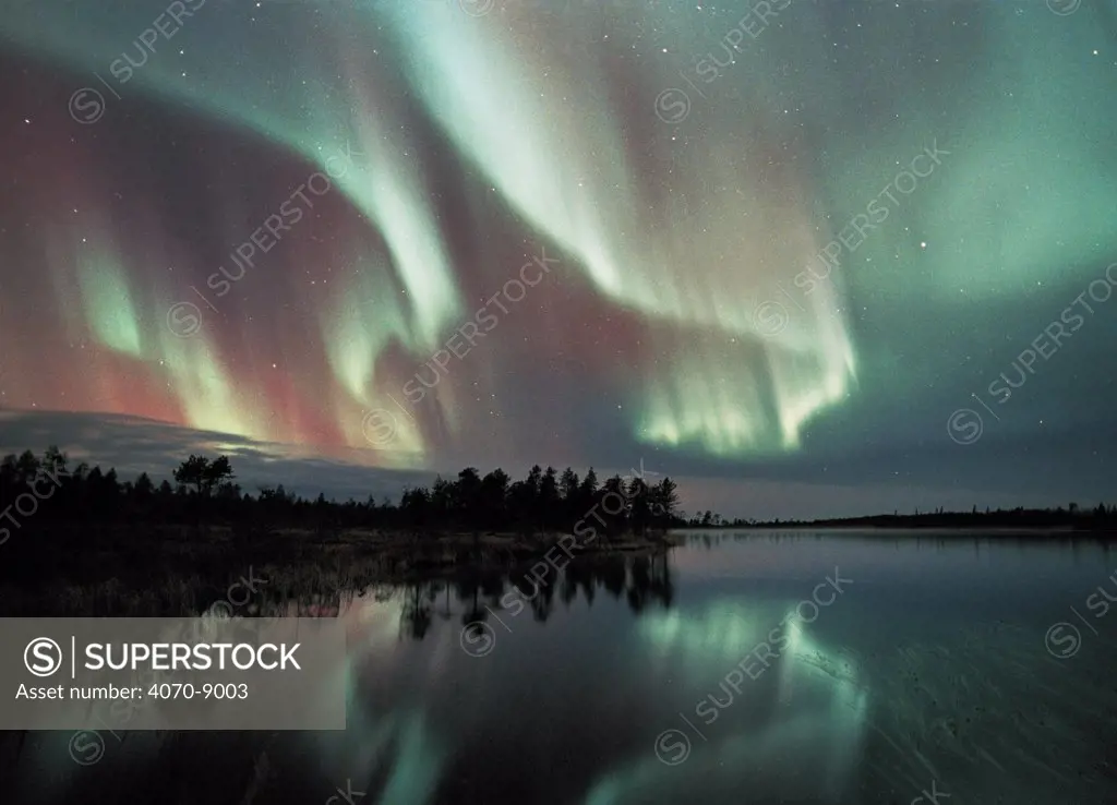 Aurora borealis colours in night sky over lake, northern Finland (nr Arctic circle), October 2002. Auroras also occur in the southern hemisphere where they are know as Aurora australis.