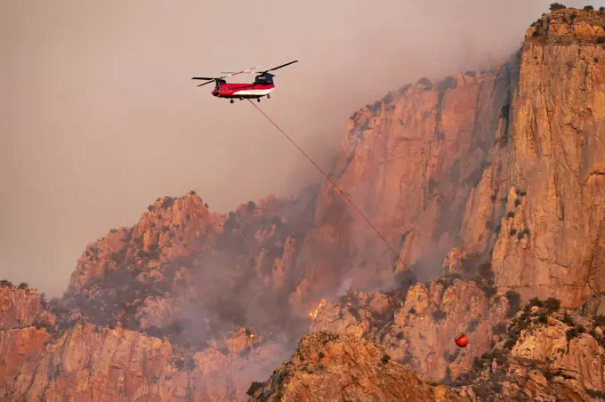 Lightning started fire on steep craggy terrain,  with  US Forest Service Fire suppression Wildland Firefighters using helicopters to 'bomb' the hot spots to control the spread. Pusch Ridge, Santa Catalina Mountains, Coronado National Forest, Arizona, USA. 6th June. June 2020.