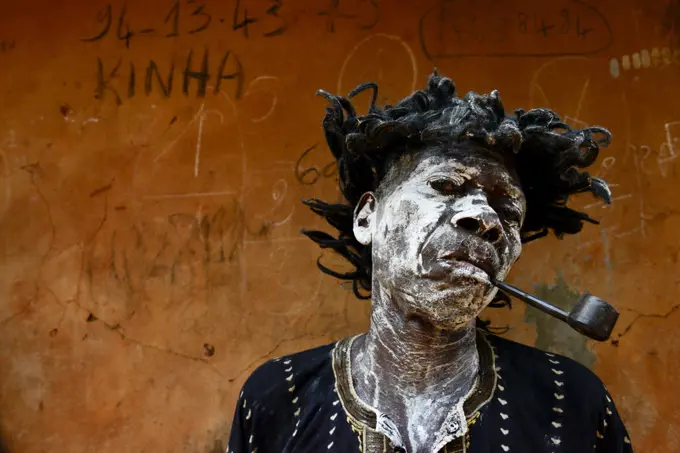 A man represents a sick and smoking character,  in a voodoo ceremony in the village of Bohicon, Benin. January 2020