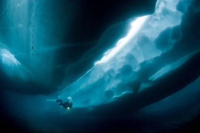 Scuba diver under and between ice formations, Lake Sassolo, Sambuco valley, Ticino, Switzerland. Model released.