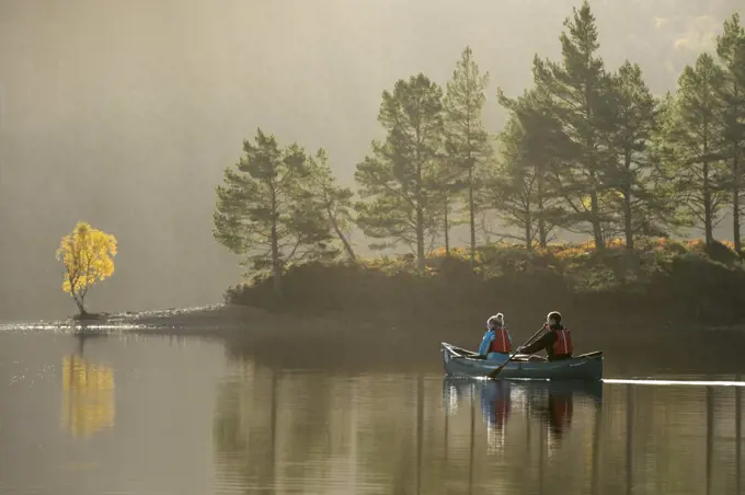 Couple canoeing on Loch Beinn a' Mheadhoin with Birch (Betula pendula) and Scots pines (Pinus sylvestris) on shore, Glen Affric, Highlands, Scotland, November 2014.