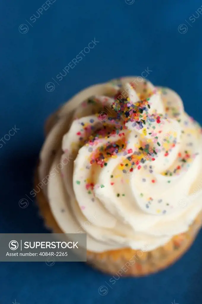 Cupcake with Vanilla Icing and Sprinkles on Blue Background