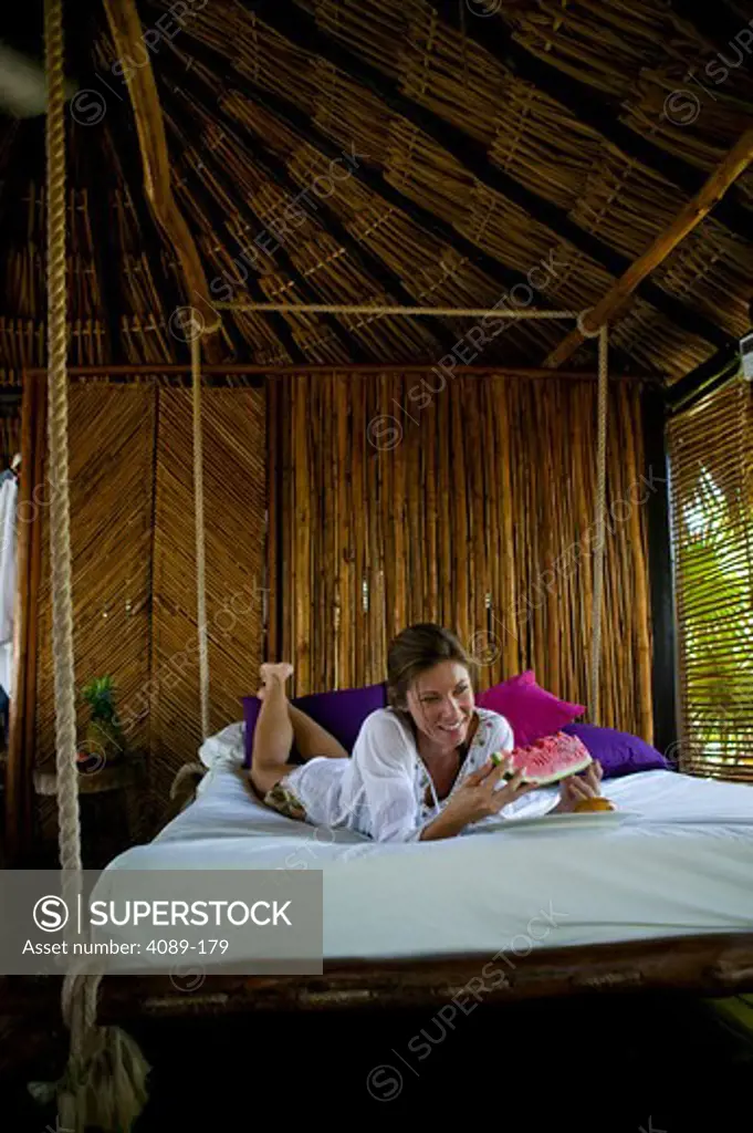 Mid adult woman lying on a hanging bed and eating watermelon in a tourist resort, Mexico