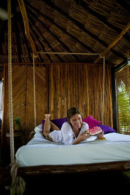 Mid adult woman lying on a hanging bed and eating watermelon in a tourist resort, Mexico