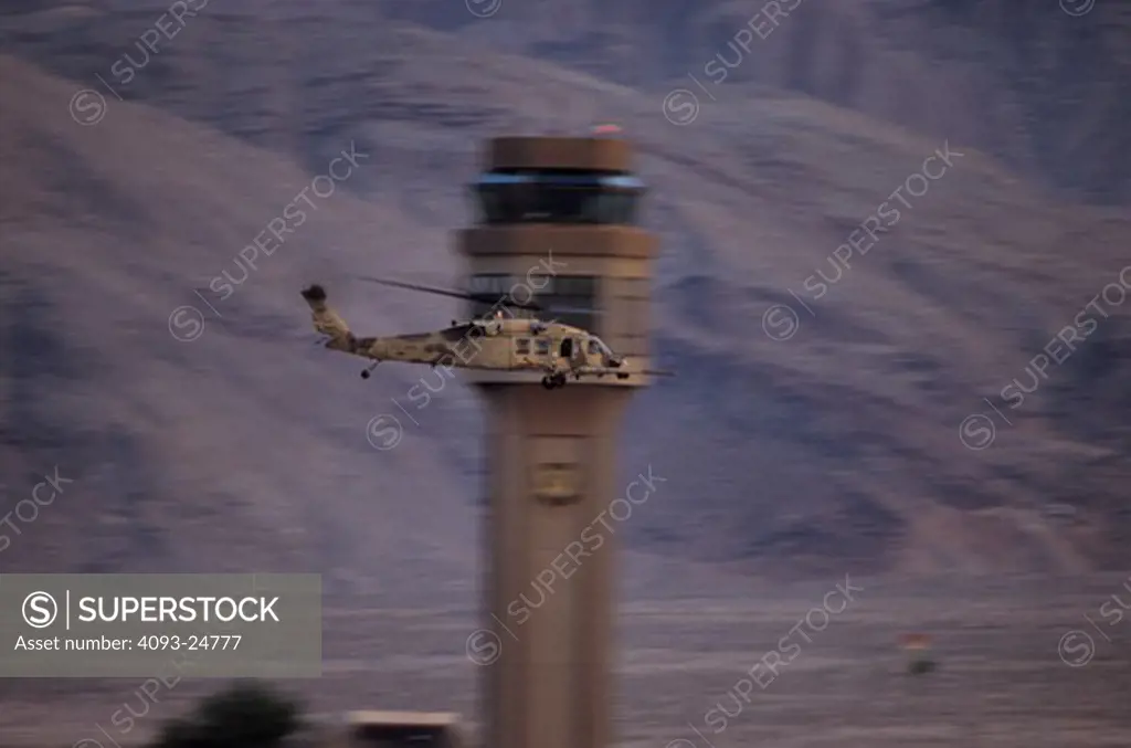 A lone USAF Sikorsky MH-60 Blackhawk combat search and rescue/special operations helicopter in an unusual desert sand camouflage paint scheme flys past the control tower at Nellis AFB, NV.