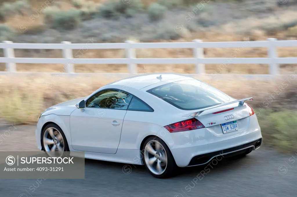 Rear 3/4 view from a high angle of a white 2012 Audi TT RS driving along a rural road.