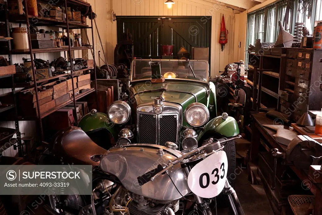 Cluttered classic car garage with 1930s MG car and Norton motorcycle.