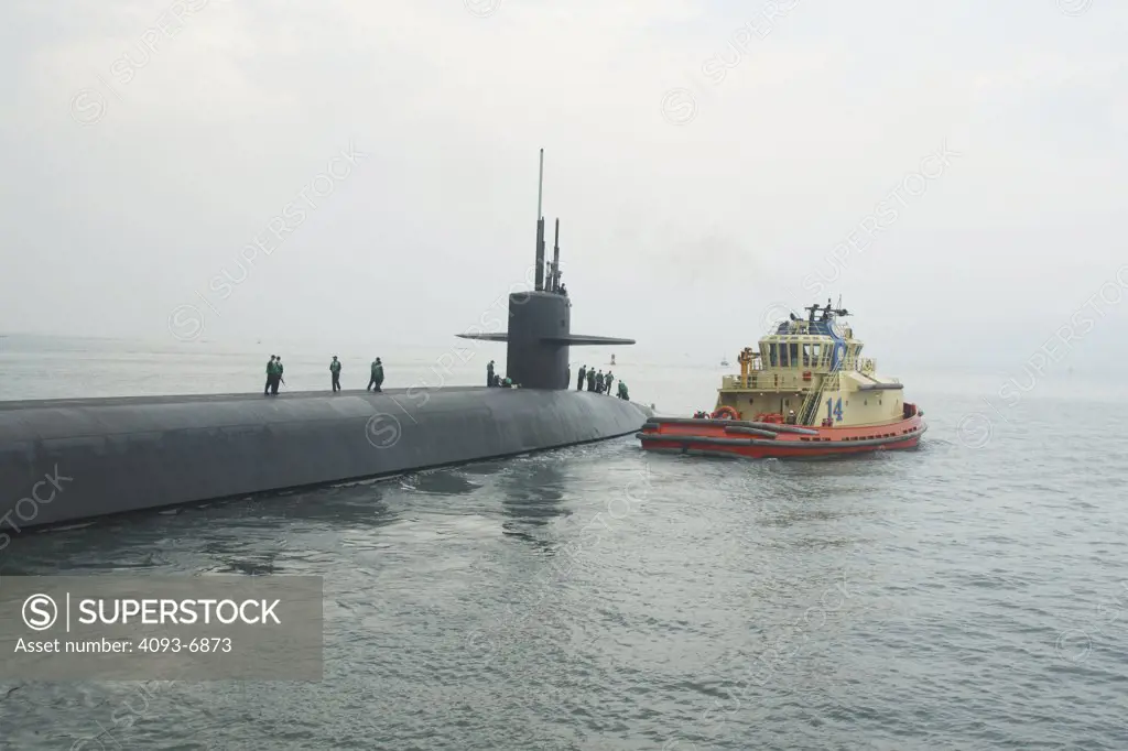 A tugboat pulls off a US Navy nuclear submarine ( boomer ) in the San Diego Bay, CA.