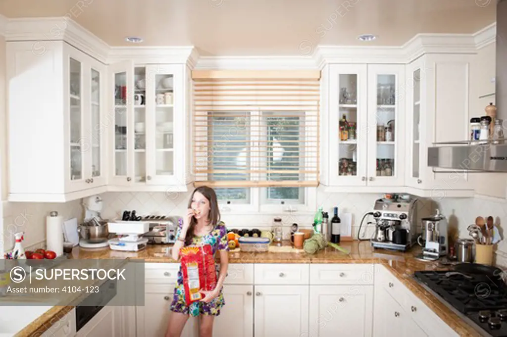 Teenage girl eating tortilla chips in the kitchen