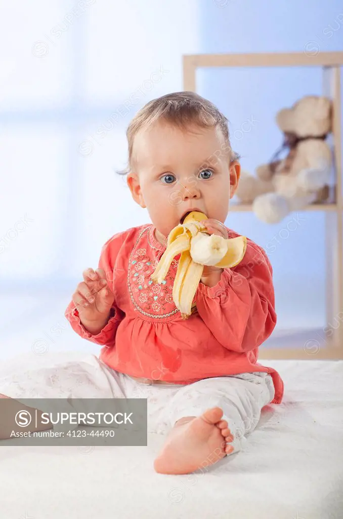 Adorable baby girl eating banana.