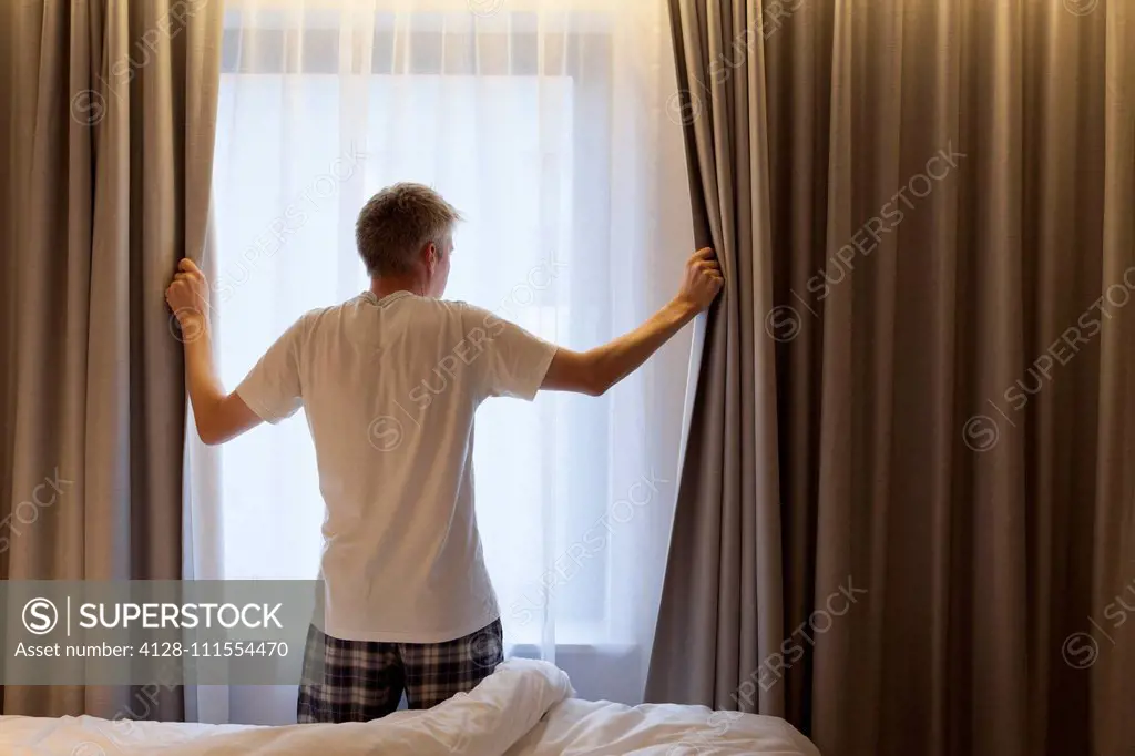 Man opening curtains in hotel room