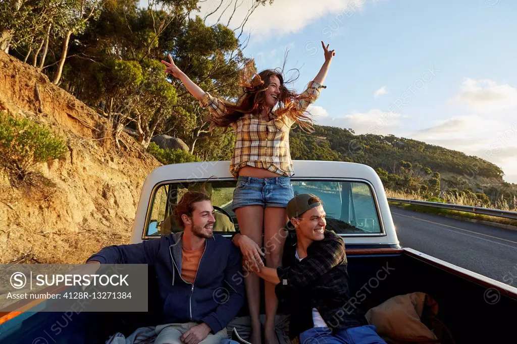 MODEL RELEASED. Young woman in pick up truck with arms raised.
