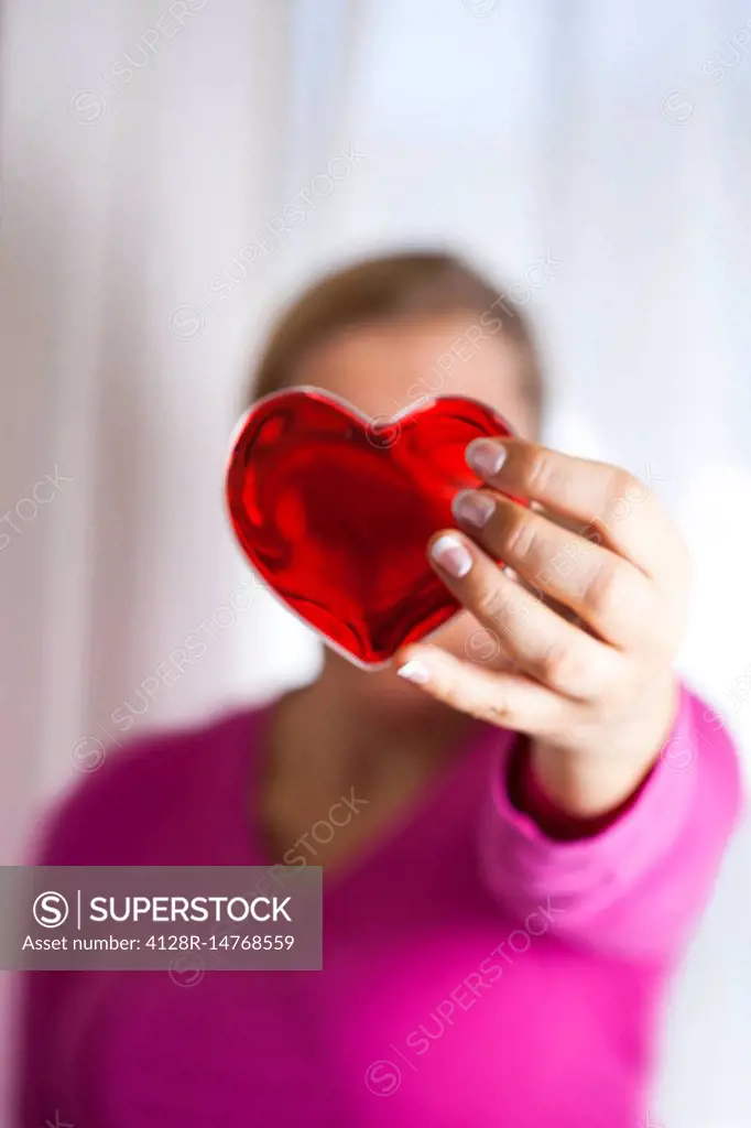 Woman holding red heart in front of her face